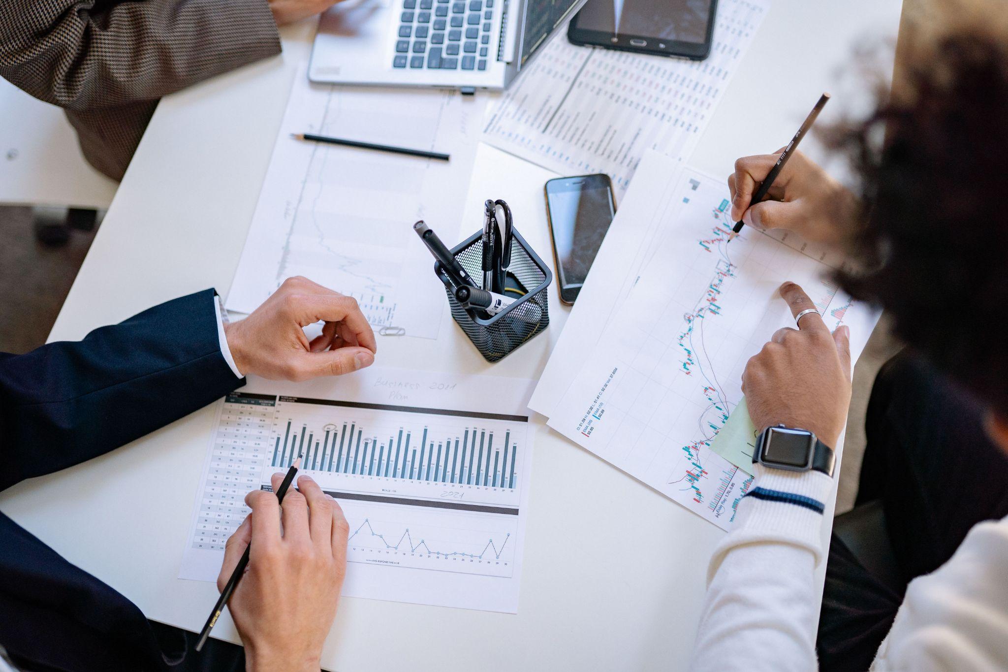 Business owners comparing hiring options and costs across printed reports at a desk
